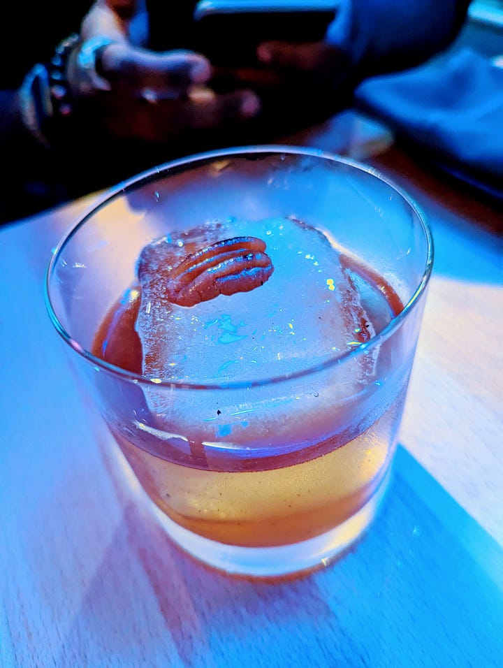 Left to right: Harana (clear drink with a lime garnish); Pecan Pie Old Fashioned (a warm light brown liquor with a pecan on top of the ice)