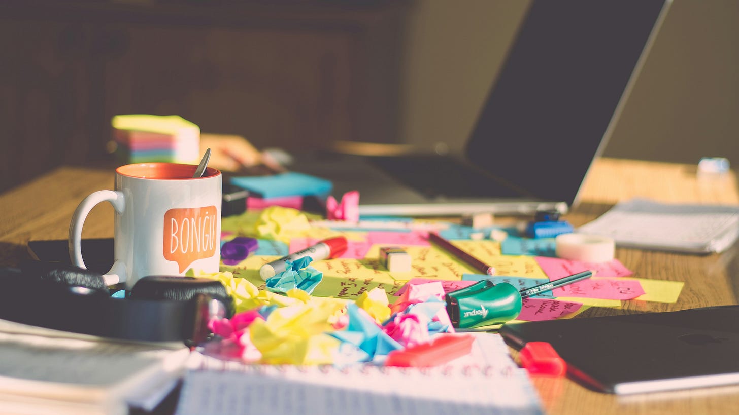 White ceramic mug on table, surrounded by crumpled sticky notes in a rainbow of colors.