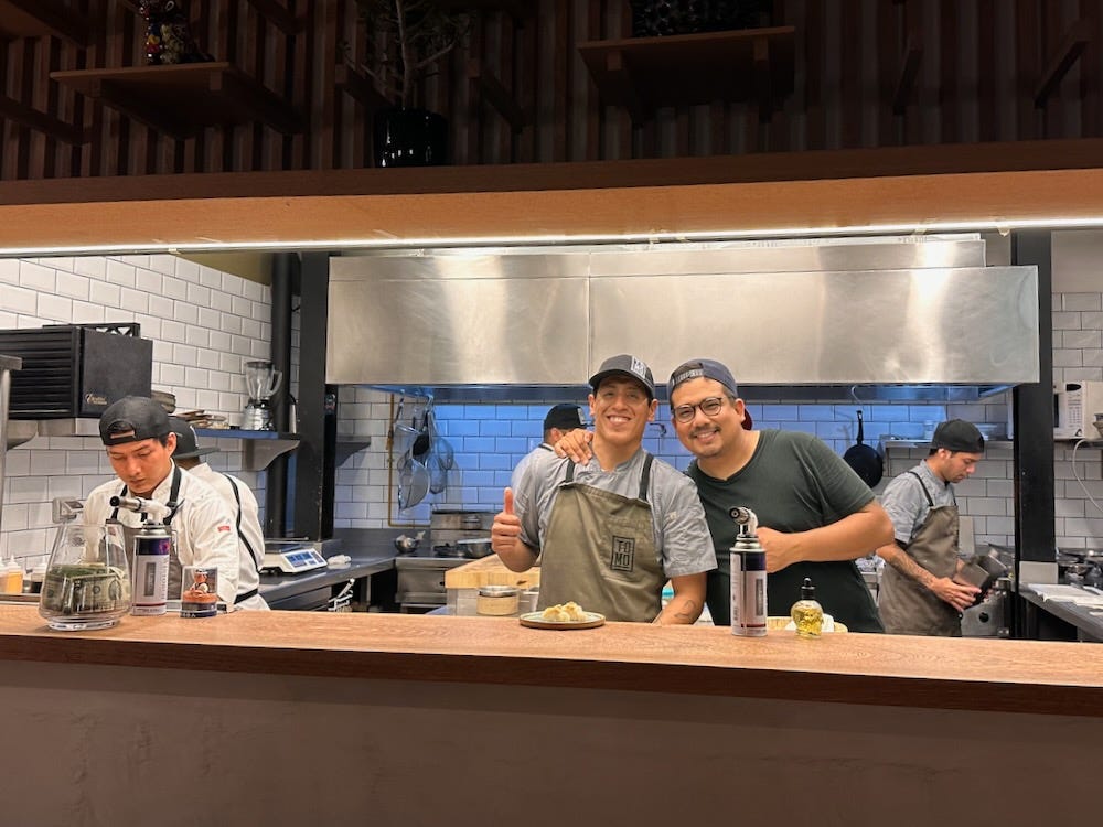 Two chefs in the middle of the open kitchen at Tomo pose for a parting photo.