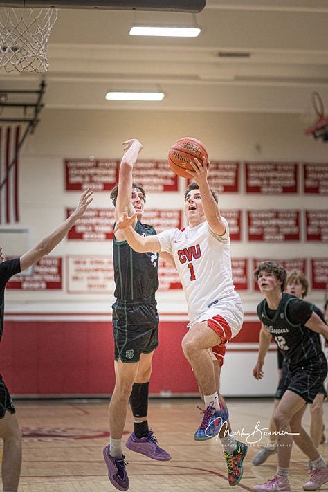 Five pictures of CVU boys basketball players in various stages of leaping and shooting with the ball. White uniforms with red lettering.