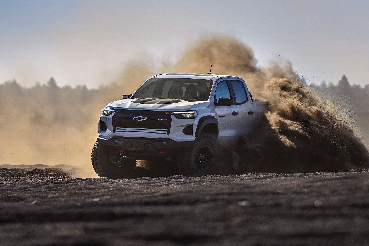 A white 2024 Chevy Colorado ZR2 Bison throws up a cloud of dirt while off-roading.