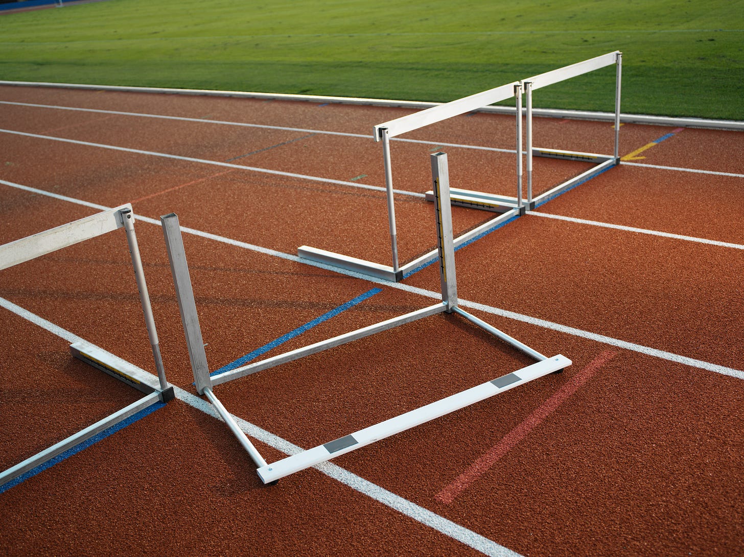 A hurdle on a competition track knocked over with pristine infield grass in the background. Photo doesn't look organic or candid, looks kinda staged