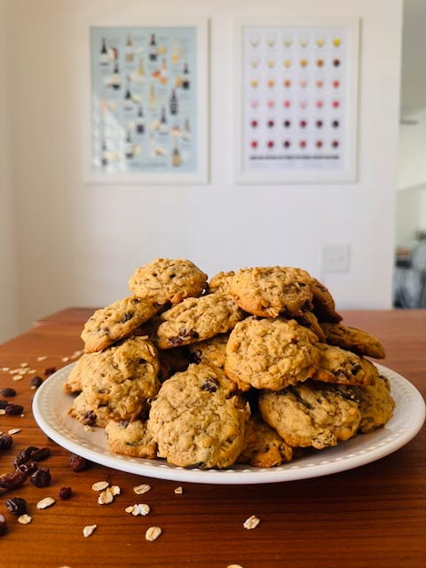 A generous plate of spicy oatmeal raisin cookies piled high on a wood table, scattered raisins and oats around it, wine posters on the wall behind A generous plate of spicy oatmeal raisin cookies piled high on a wood table, scattered raisins and oats around it, wine posters on the wall behind