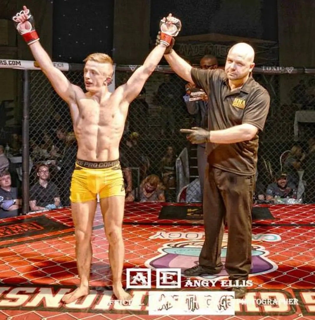A professional photo from a MMA fight with Craig, a blond man with yellow shorts, holding has hands up in victory by a referee, in a cage, there is a cheering audience in the background