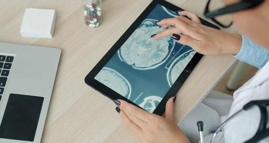 Doctor examining brain scan on tablet at desk. Doctor examining brain scan on tablet at desk.