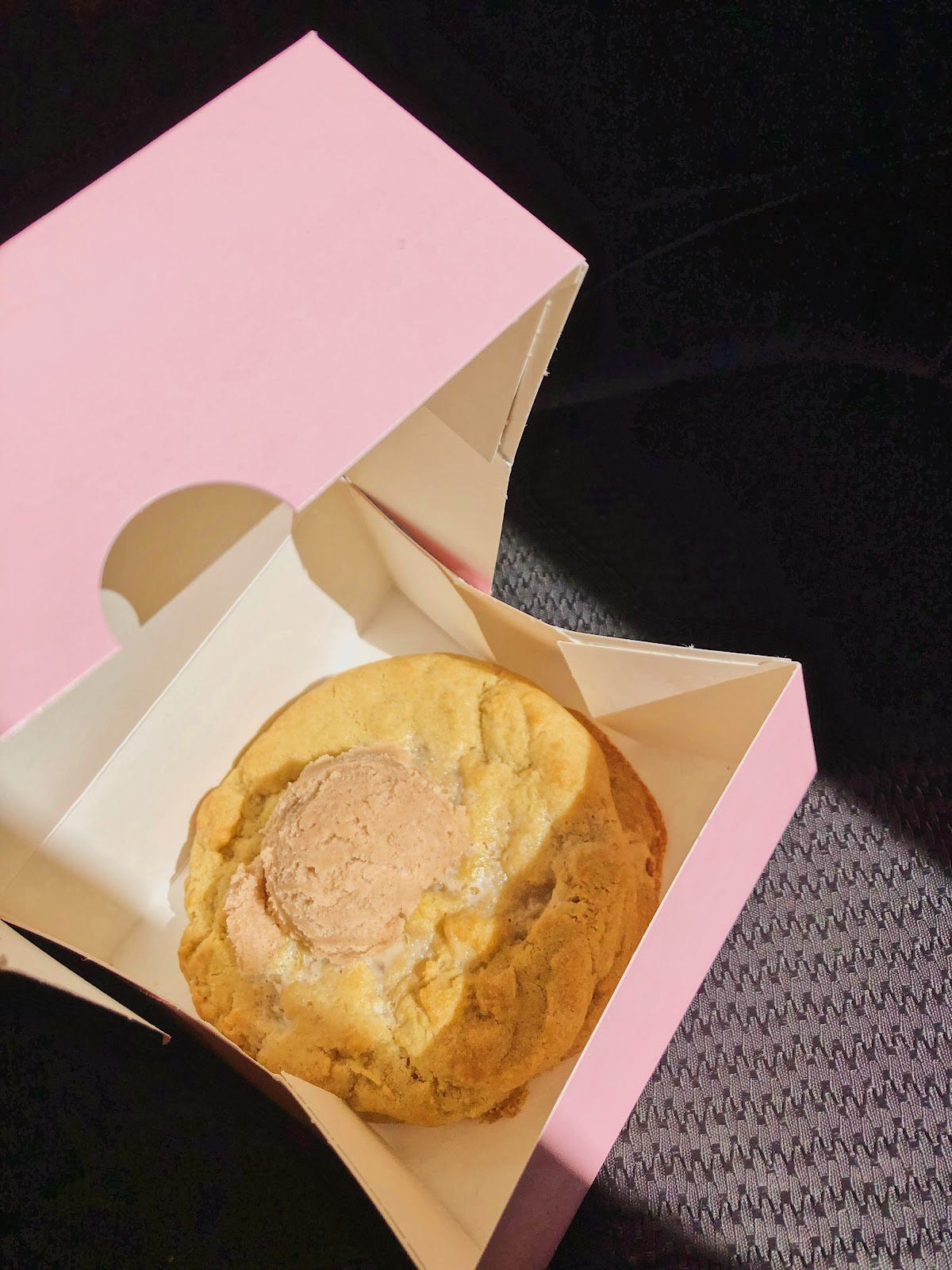 A pink Crumbl cookie box opened, with a buttery thick cookie with cinnamon on top.