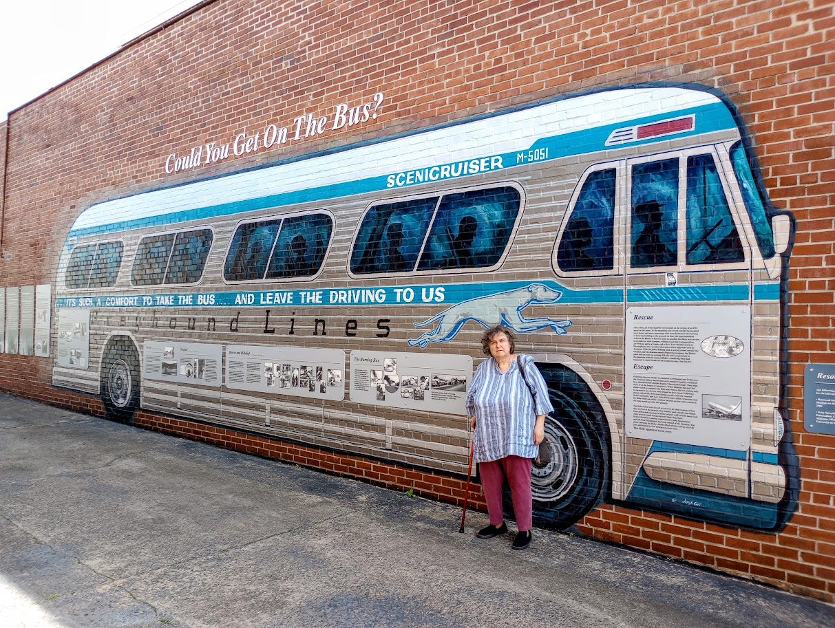 Annette in front of life-size miral of Greyhound bus in brick alley