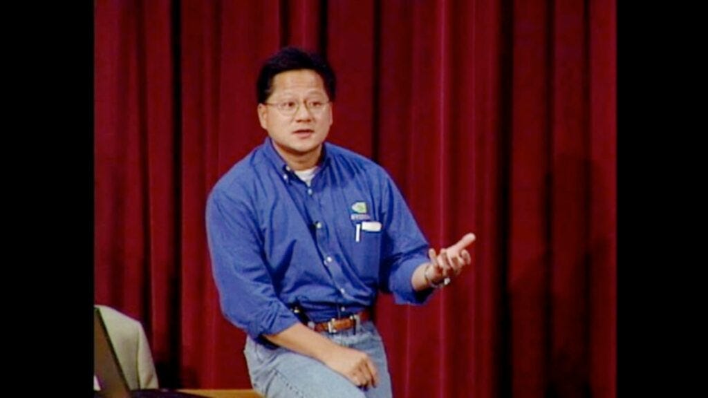 A younger Jensen Huang speaking on stage in casual attire.