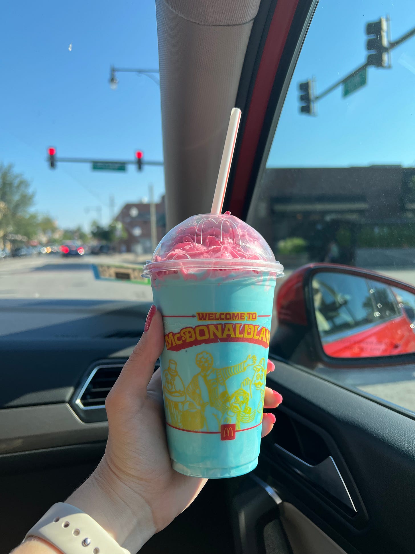 Blue McDonaldland shake with pink whipped topping; it's inside a car and the street can be seen behind