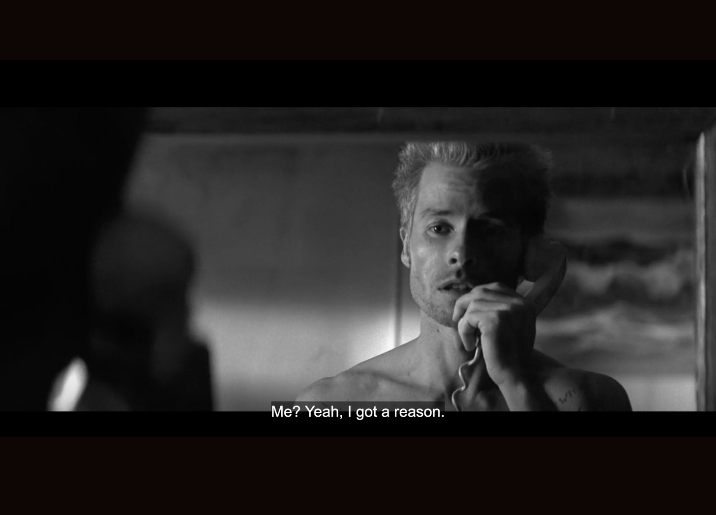 Leonard in a hotel room, looking at a mirror, saying: "Me? Yeah, I got a reason." He is talking on the phone.