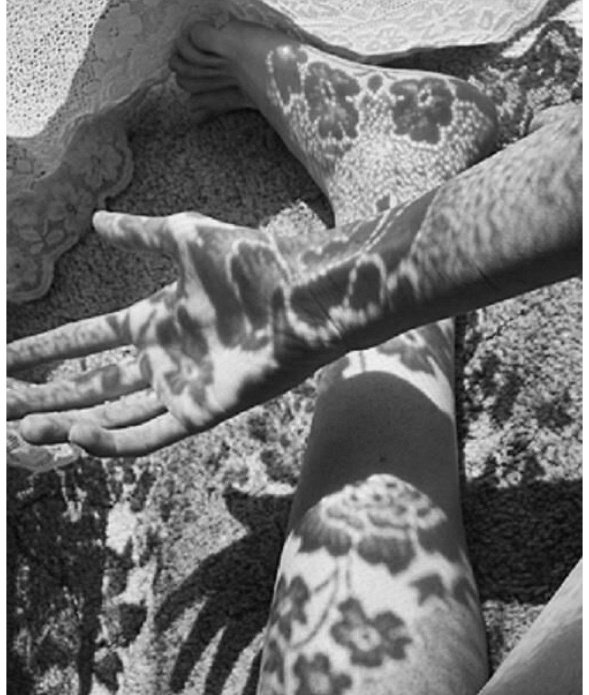 Black-and-white image of a woman seated on the floor, lace shadows softening her skin with patterned light.