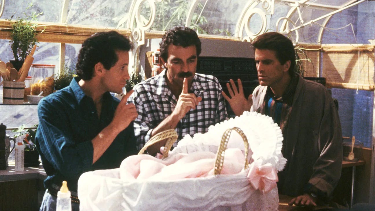 A scene from the 1987 film Three Men and a Baby showing three men — one in a blue shirt, one in a plaid shirt with a mustache, and one in a gray robe — huddled together with concerned expressions around a baby in a white wicker bassinet decorated with pink ruffles and a bow. A scene from the 1987 film Three Men and a Baby showing three men — one in a blue shirt, one in a plaid shirt with a mustache, and one in a gray robe — huddled together with concerned expressions around a baby in a white wicker bassinet decorated with pink ruffles and a bow.