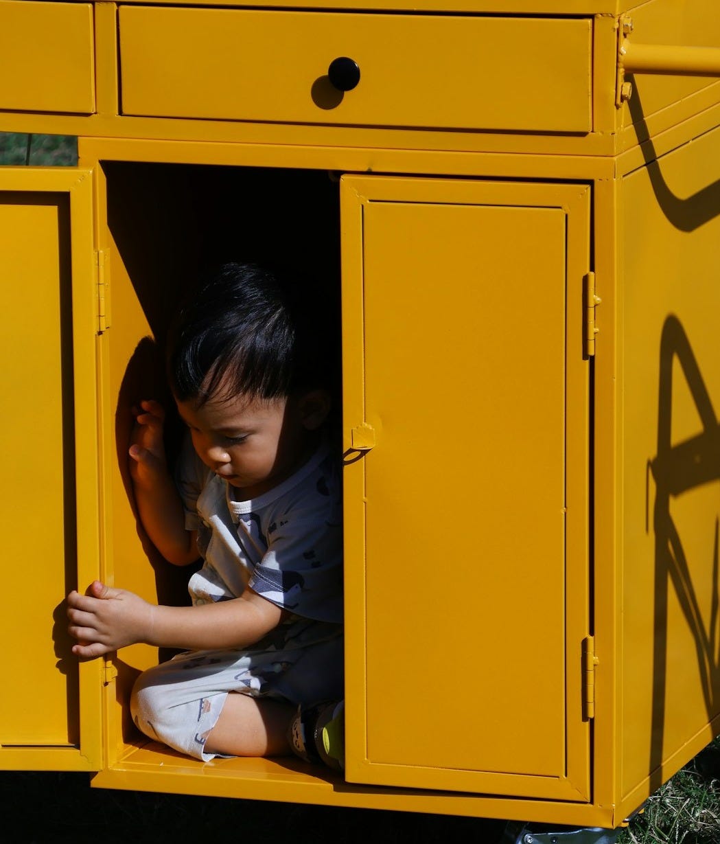 Young child sitting inside a yellow cabinet outdoors cart
