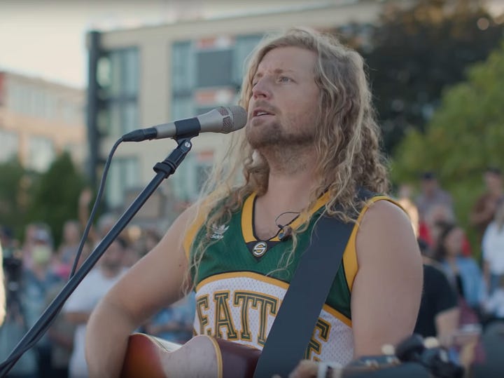 1. Long haired blond Christian performer Sean Feucht with his guitar in concert. 2. Long-dreadlocked, bearded and tattooed punk-rap performer Pascal Robinson-Foster of Bob Vylan, on the mic in concert.