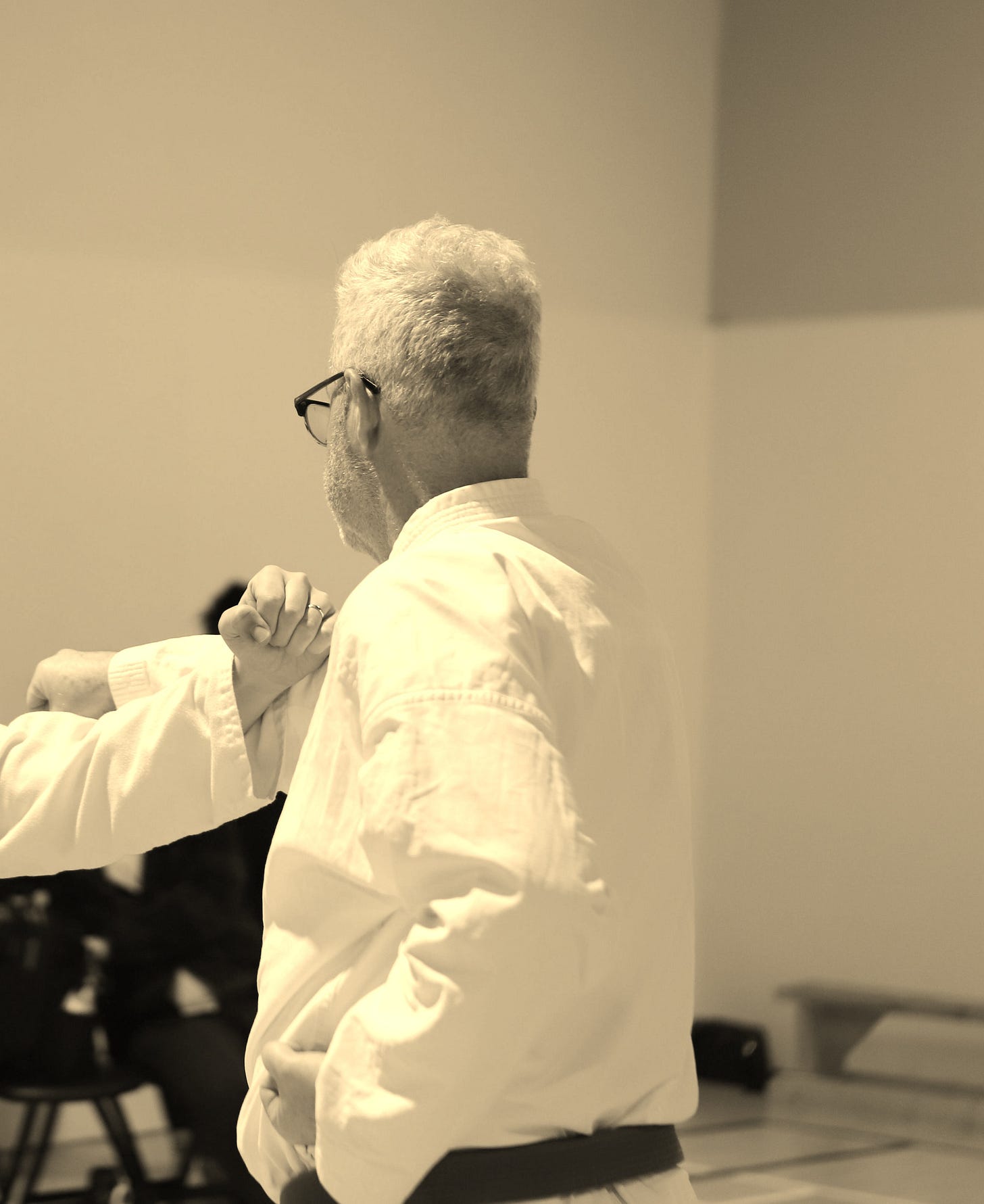 An individual in athletic gear (a "gi") performing a specific movement in a brightly lit gymnasium during a regional competition.