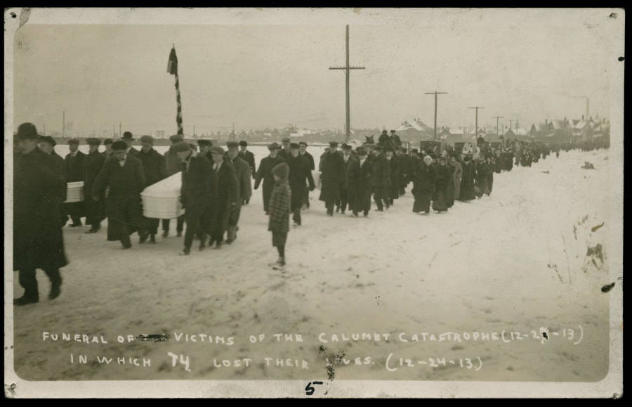 A haunting black and white photograph of the 1913 funeral procession. Hundreds of mourners line the snowy streets of Calumet as a long line of coffins is carried toward Lake View Cemetery.