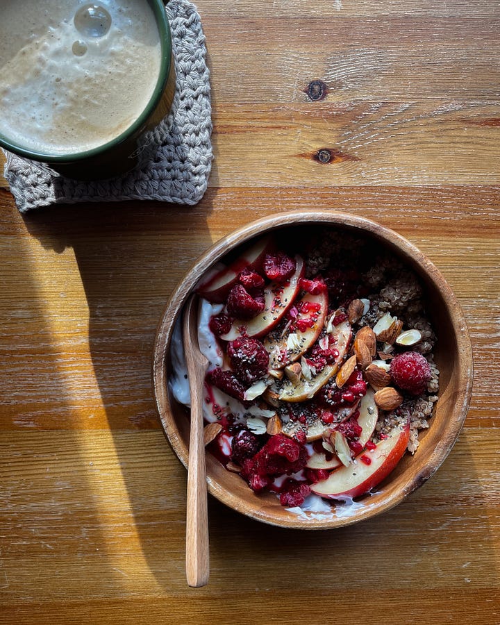 Gallery with 2 images. Image 1: A sunny breakfast desk scene with my cinnamon quinoa bowl and morning coffee. / Image 2: A close-up of raspberries, nectarines, almonds, and yoghurt-topped quinoa glowing in the sun.
