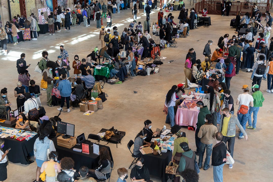 A long room filled with people vending and checking out the vendors. Everyone is wearing masks. 