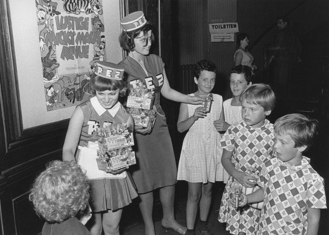 Two young women give away PEZ dispensers to sets of twins in a movie theater lobby in Germany in 1964.