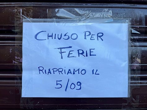 Chiuso per ferie, handwritten signs saying the shops are closed for the month of August and overgrown plants on the sidewalk