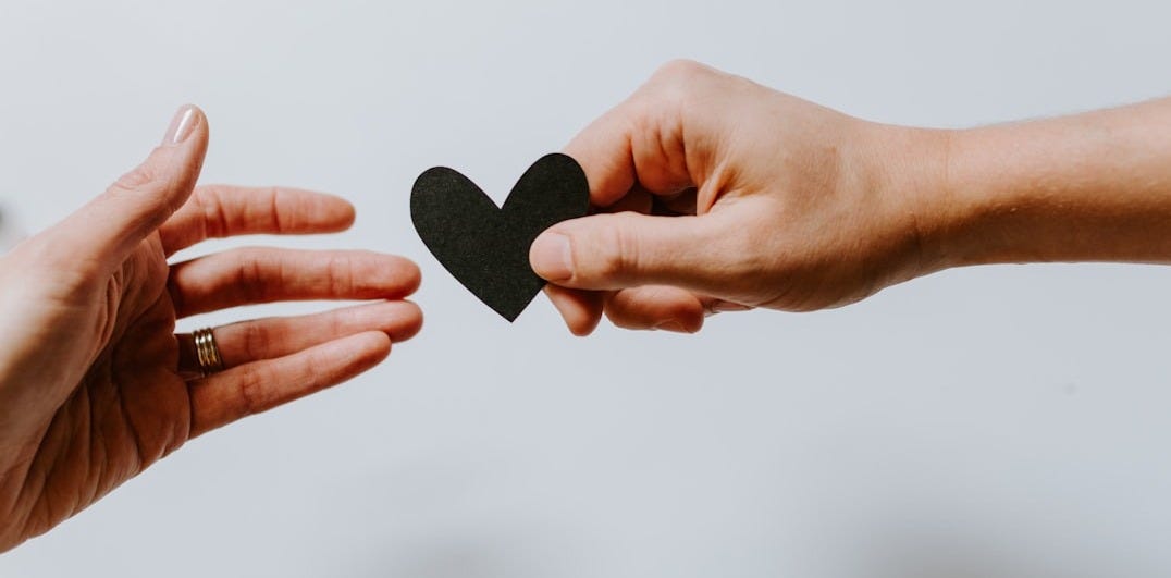 person reaching black heart cutout paper