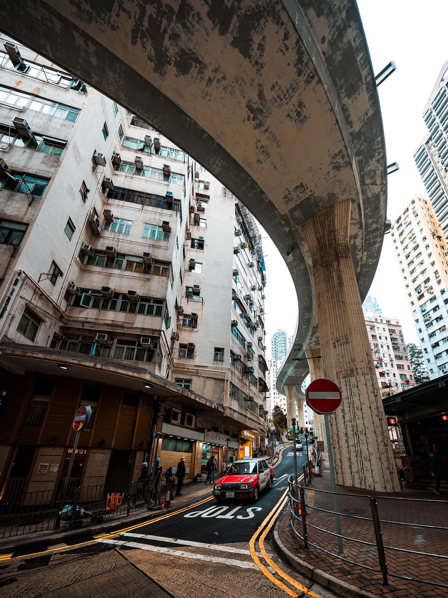 Hill Road Flyover in Shek Tong Tsui, Hong Kong, curving above a narrow street with a red taxi Hill Road Flyover in Shek Tong Tsui, Hong Kong, curving above a narrow street with a red taxi