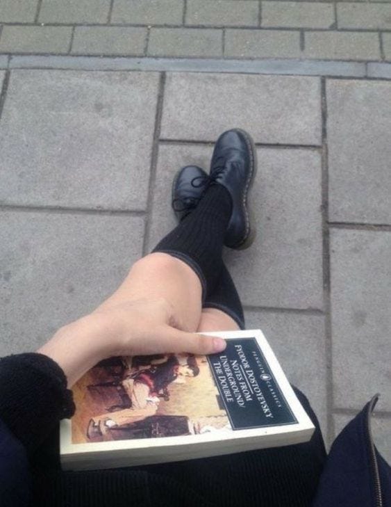 This may contain: a person sitting on the ground with their feet up and holding a book in front of them