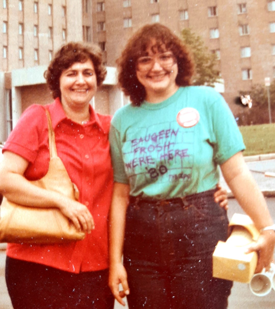 Photo of Janine on the left, wearing a university residence t-shirt, funky 80's glasses, with shoulder length permed hair. Her mom on the left, smiling at the camera Photo of Janine on the left, wearing a university residence t-shirt, funky 80's glasses, with shoulder length permed hair. Her mom on the left, smiling at the camera