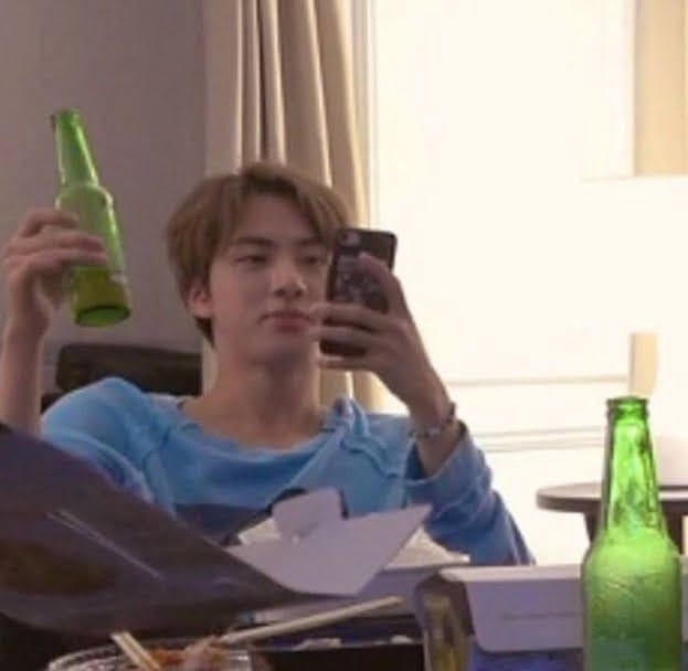 Kim Seokjin of BTS holding a beer bottle while reading his cellphone