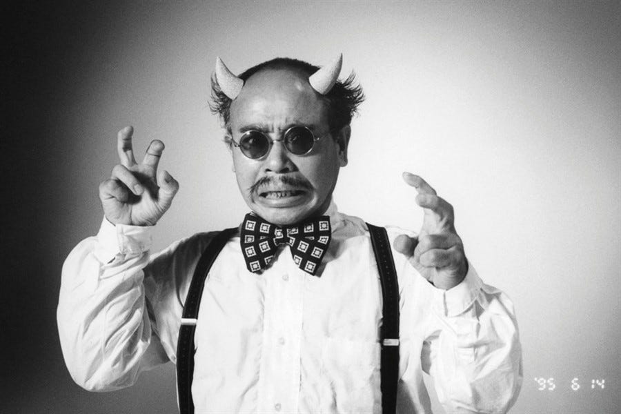 A man wearing sunglasses, fake horns, a bow-tie, and suspenders making a goofy growling expression. A man wearing sunglasses, fake horns, a bow-tie, and suspenders making a goofy growling expression.