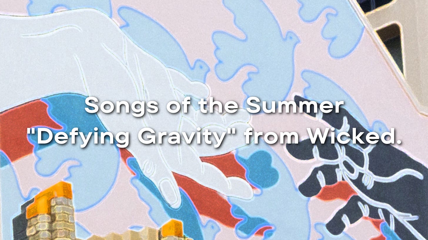 Graffiti along a large wall. The bottom has gold stones as the foundation of an incomplete wall. The top has two huge hands reaching out to each other in the foreground (one white acrylic color and one black acrylic color, both casting red shadows behind the background). The background is pink with blue dove outlines flying in a tiled pattern.   At the bottom is the text: 'Songs of the Summer: "Defying Gravity" from Wicked.'