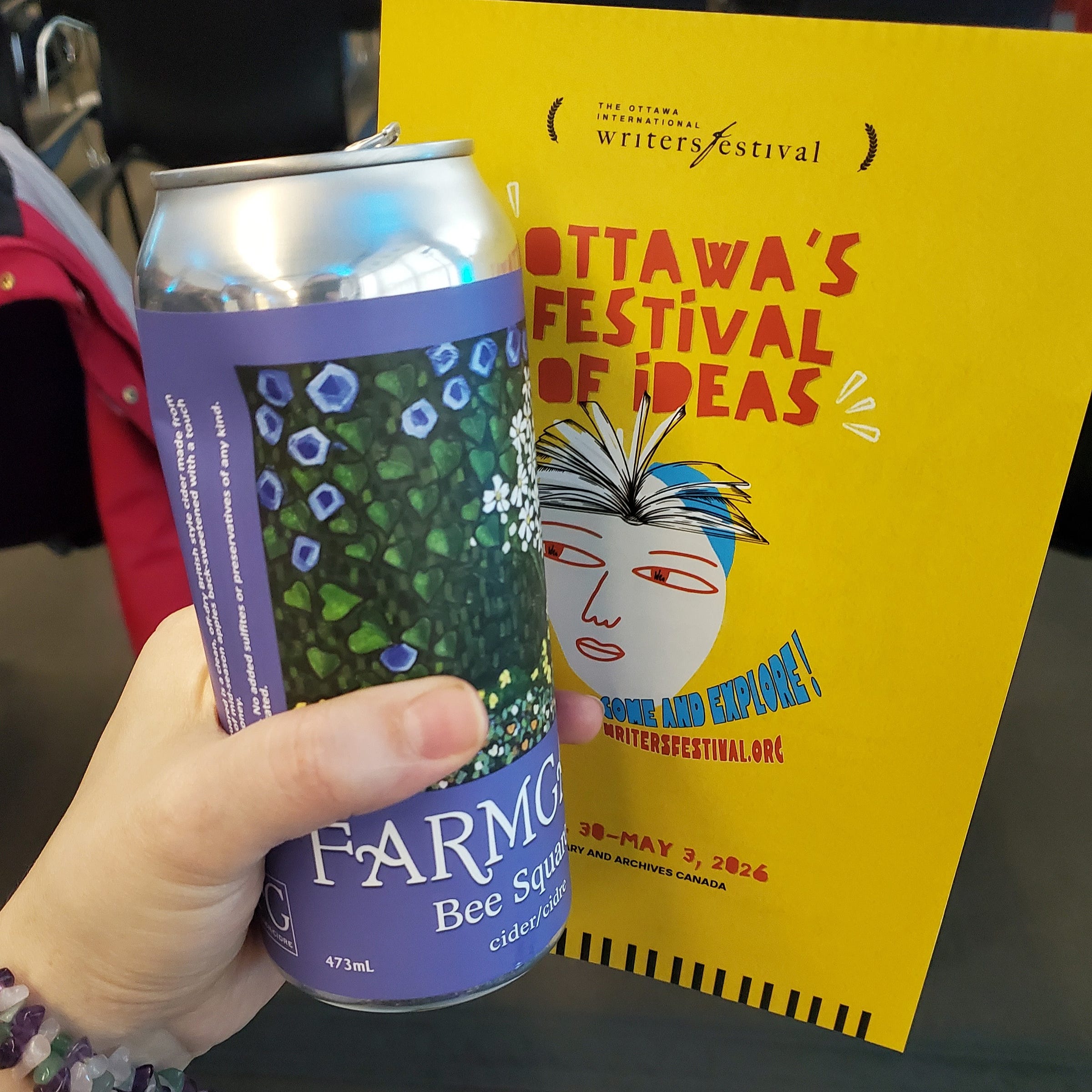 A hand hold a can of cider and the Writer's Festival program.