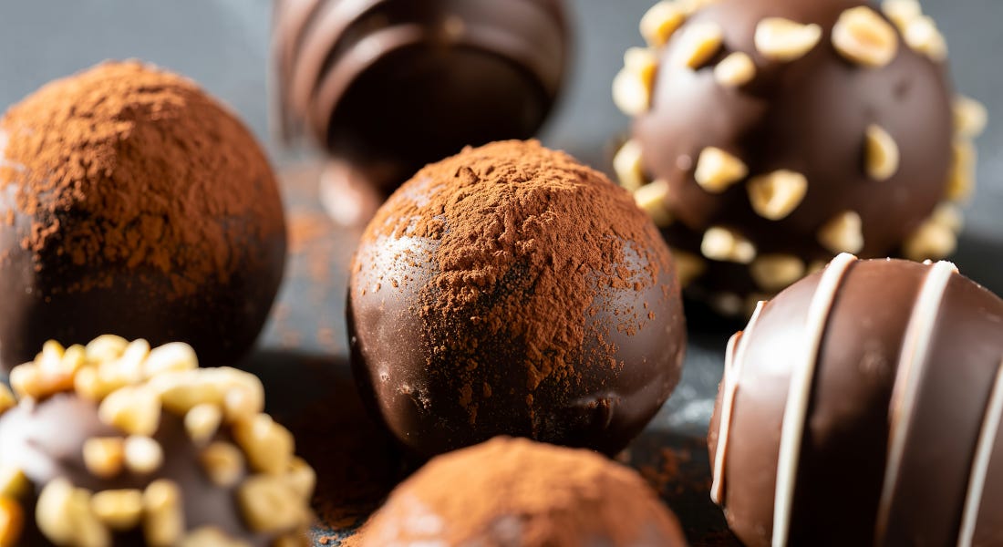 A close-up of seven truffles with cocoa dusting, chocolate drizzle, and hazelnut toppings