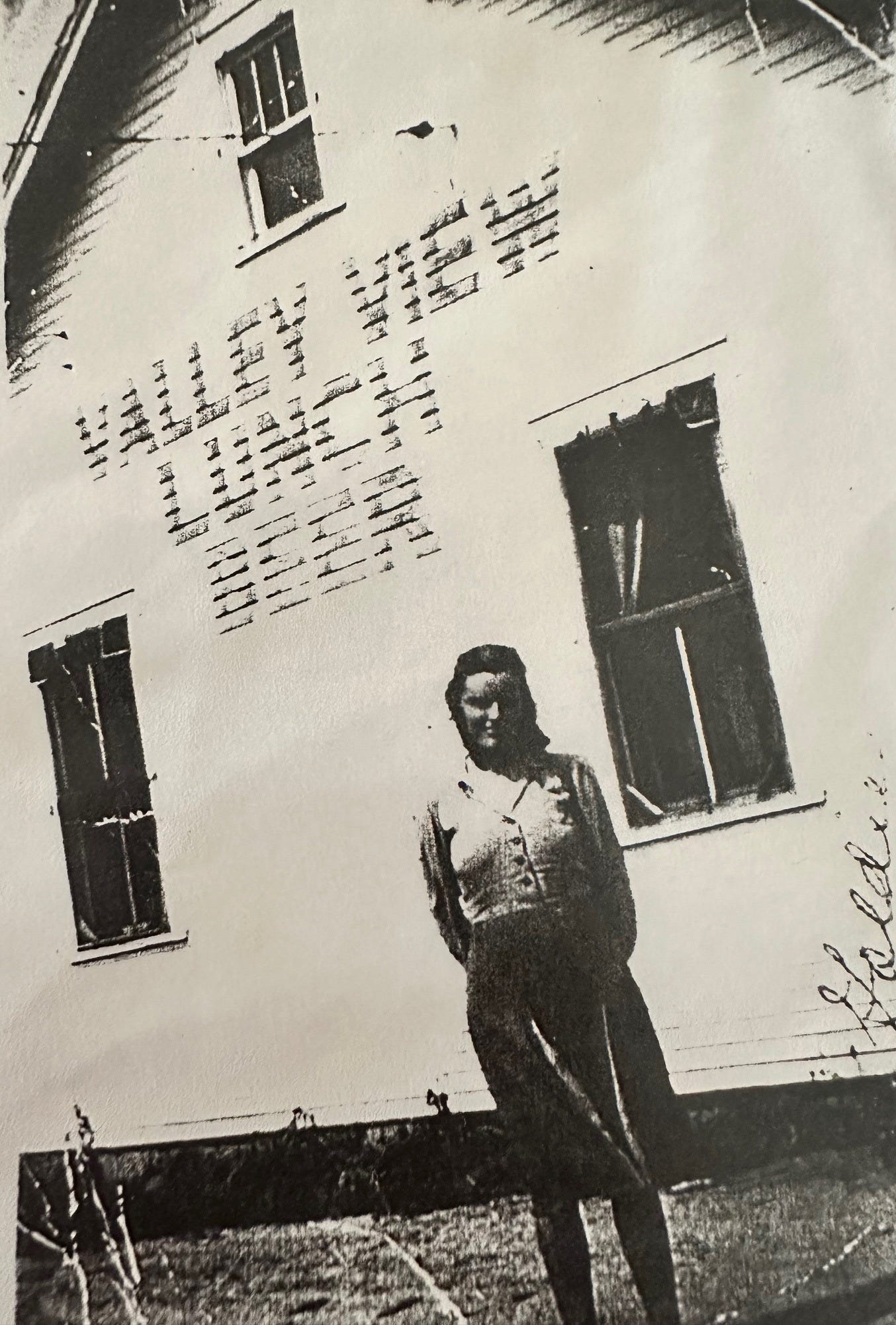 A young woman from the 1930s stands in front of a white building with the words "Valley View Lunch & Beer" stenciled on the side