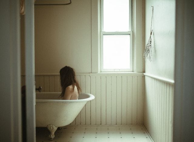 This may contain: a woman is sitting in the bathtub with her head on the window sill