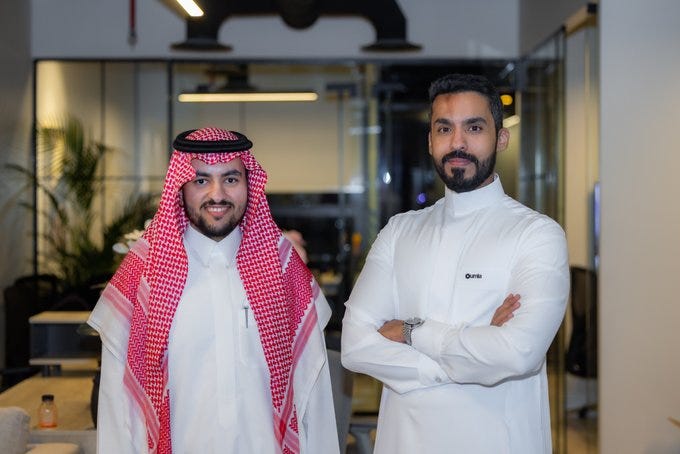 Mohammad Al-Jaser and Salah Al-Salman standing side by side in a modern office. Mohammad Al-Jaser wears a white thobe and a red-and-white checkered ghutra with a black agal. Salah Al-Salman wears a white thobe with a small logo on the chest, arms crossed.