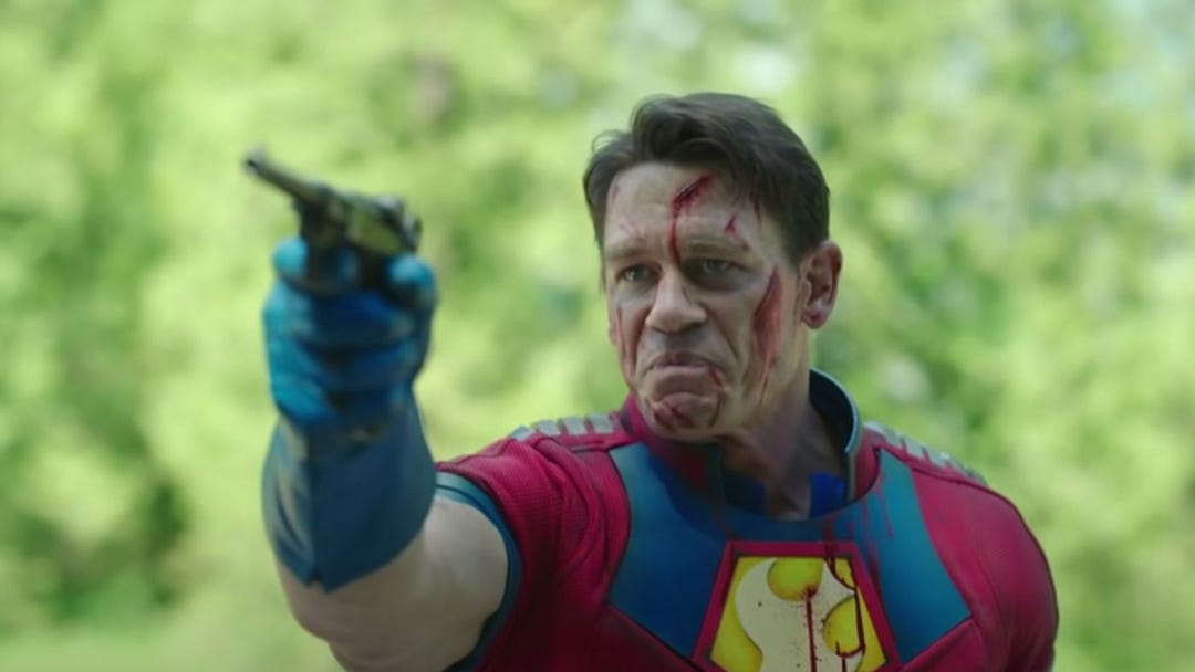 peacemaker looking sad with blood on his face pointing a gun in a woods