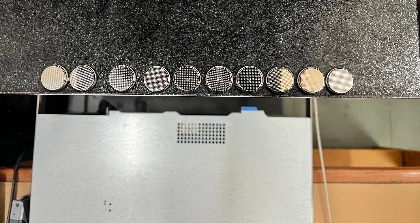 en metallic coin-cell CR2032 batteries lined up in a row on top of a dusty black computer server chassis.