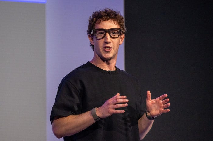 Mark Zuckerberg wearing Meta Ray-Ban Display AI glasses and a black shirt, gesturing while speaking.