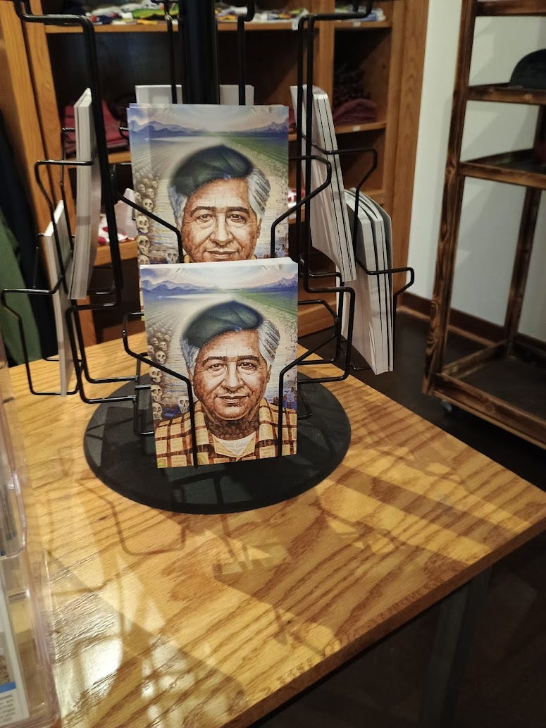 Postcards of Cesar Chavez in rack in gift shop. Behind his image, skulls in an empty field with mountains in background