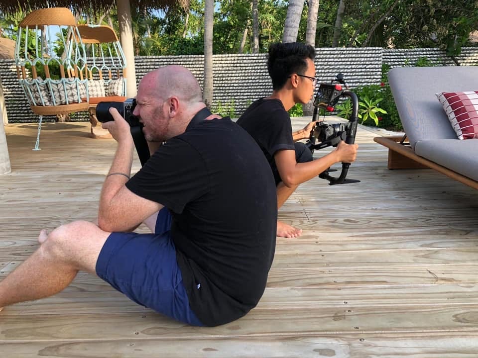 A stills photographer and videographer working back to back on an outdoor deck