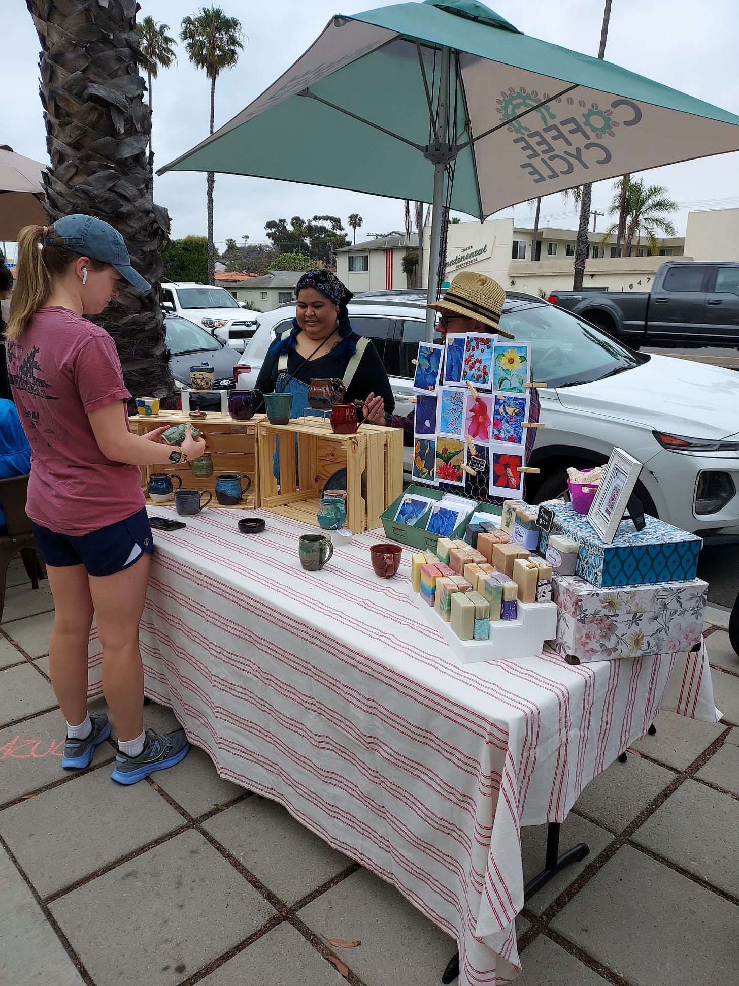 A jogger stops to admire handmade clay mugs and homemade soaps at a makers market on a SoCal sidewalk. A jogger stops to admire handmade clay mugs and homemade soaps at a makers market on a SoCal sidewalk.