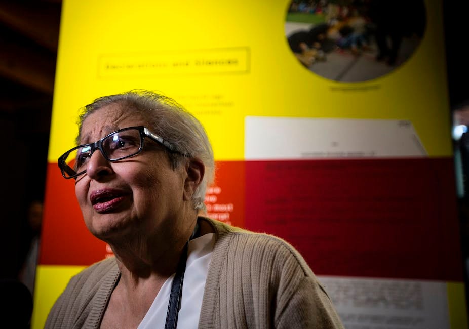 An elderly Indian woman with glasses and grey hair looks earnest as she speaks. An elderly Indian woman with glasses and grey hair looks earnest as she speaks.