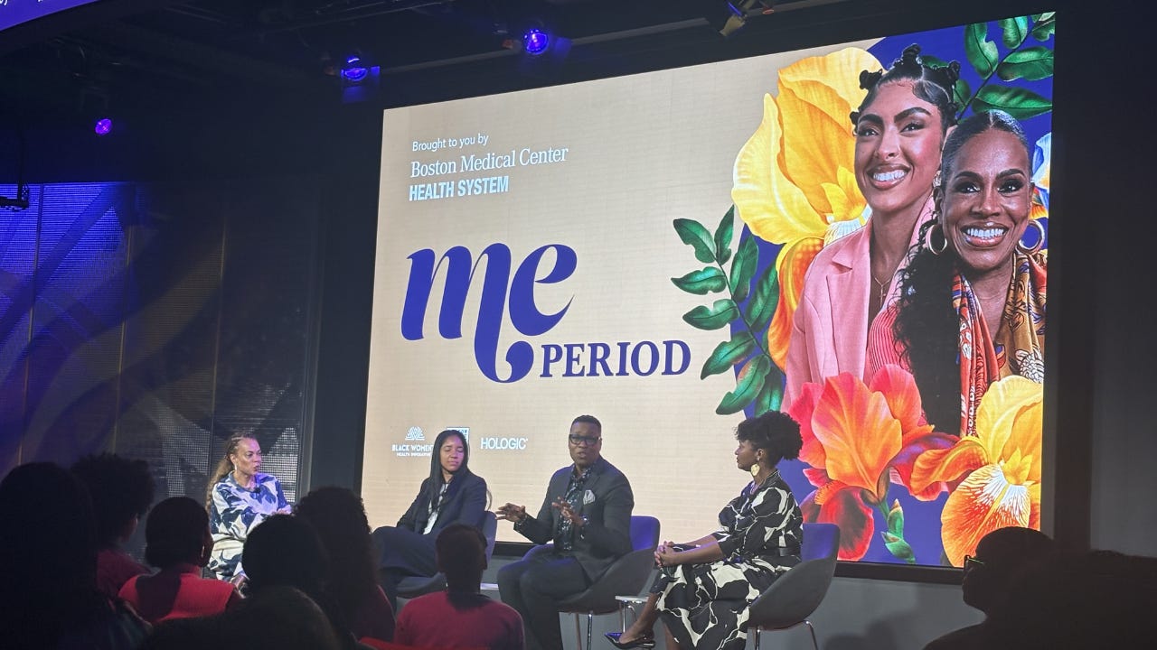 Four speakers sit in chairs facing an audience while a large screen behind them displays the event title alongside colorful floral graphics and portraits of two smiling women.