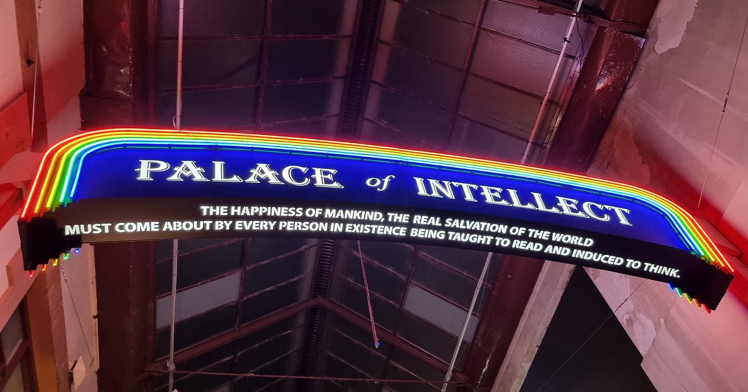 A rainbow sign reads Palace of Intellect. The happiness of mankind, the real salvation of the world must come about by every person in existence being taught to read and induced to think" A rainbow sign reads Palace of Intellect. The happiness of mankind, the real salvation of the world must come about by every person in existence being taught to read and induced to think"