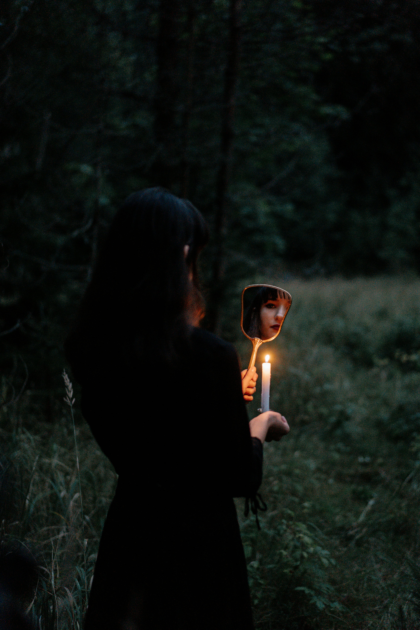 Woman in Black Long Sleeves Dress Holding a Mirror and a Lighted Candle