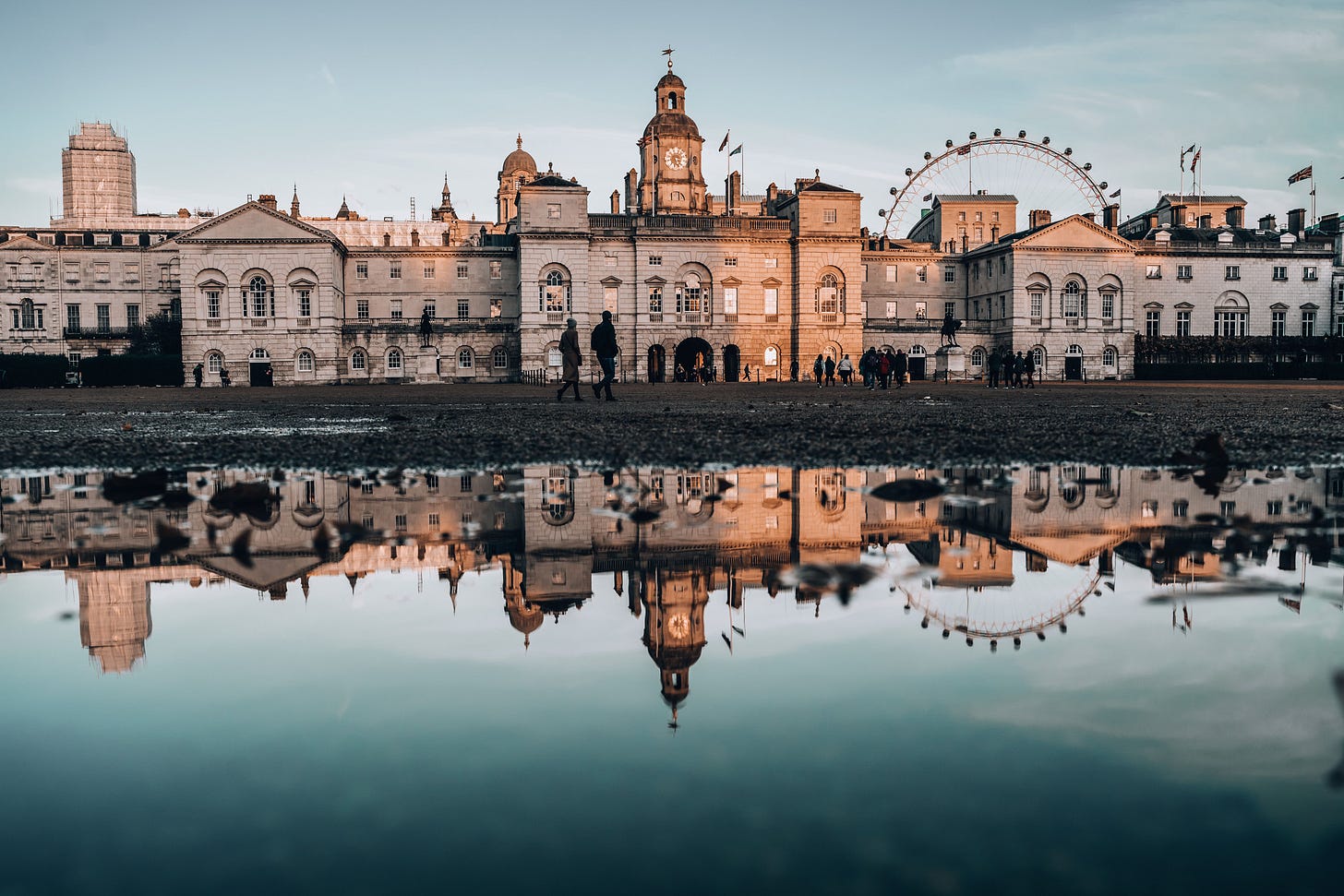 Captivating reflection of Horse Guards Parade in central London, with the historic government buildings mirrored in a puddle and the London Eye rising in the background during a calm evening.