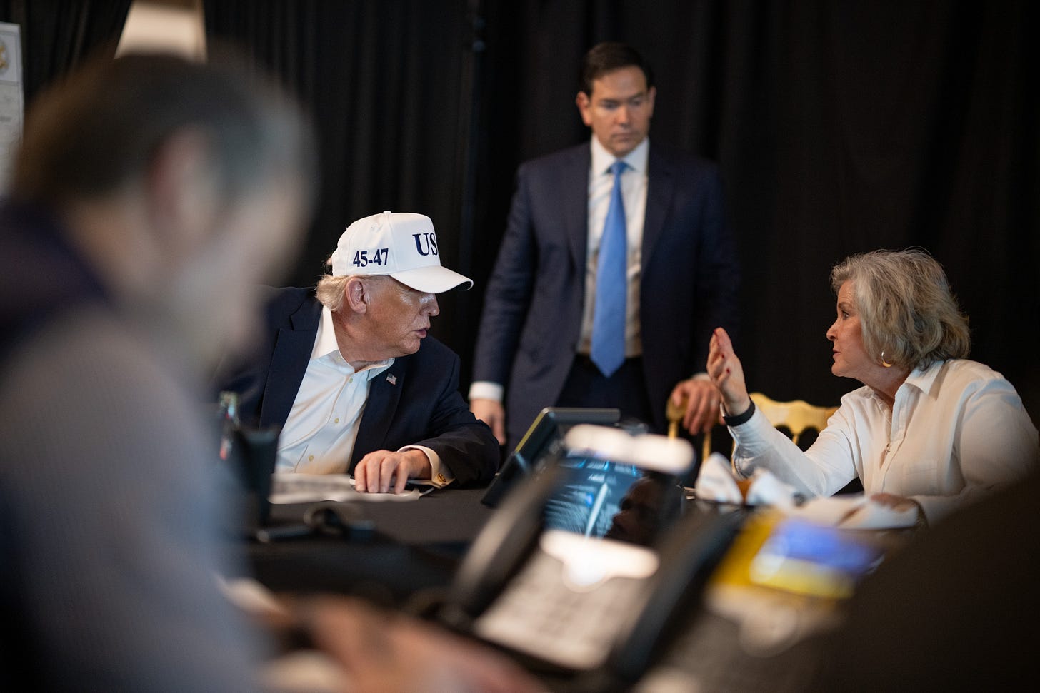 Trump talks to a woman while wearing a white USA baseball cap Trump talks to a woman while wearing a white USA baseball cap