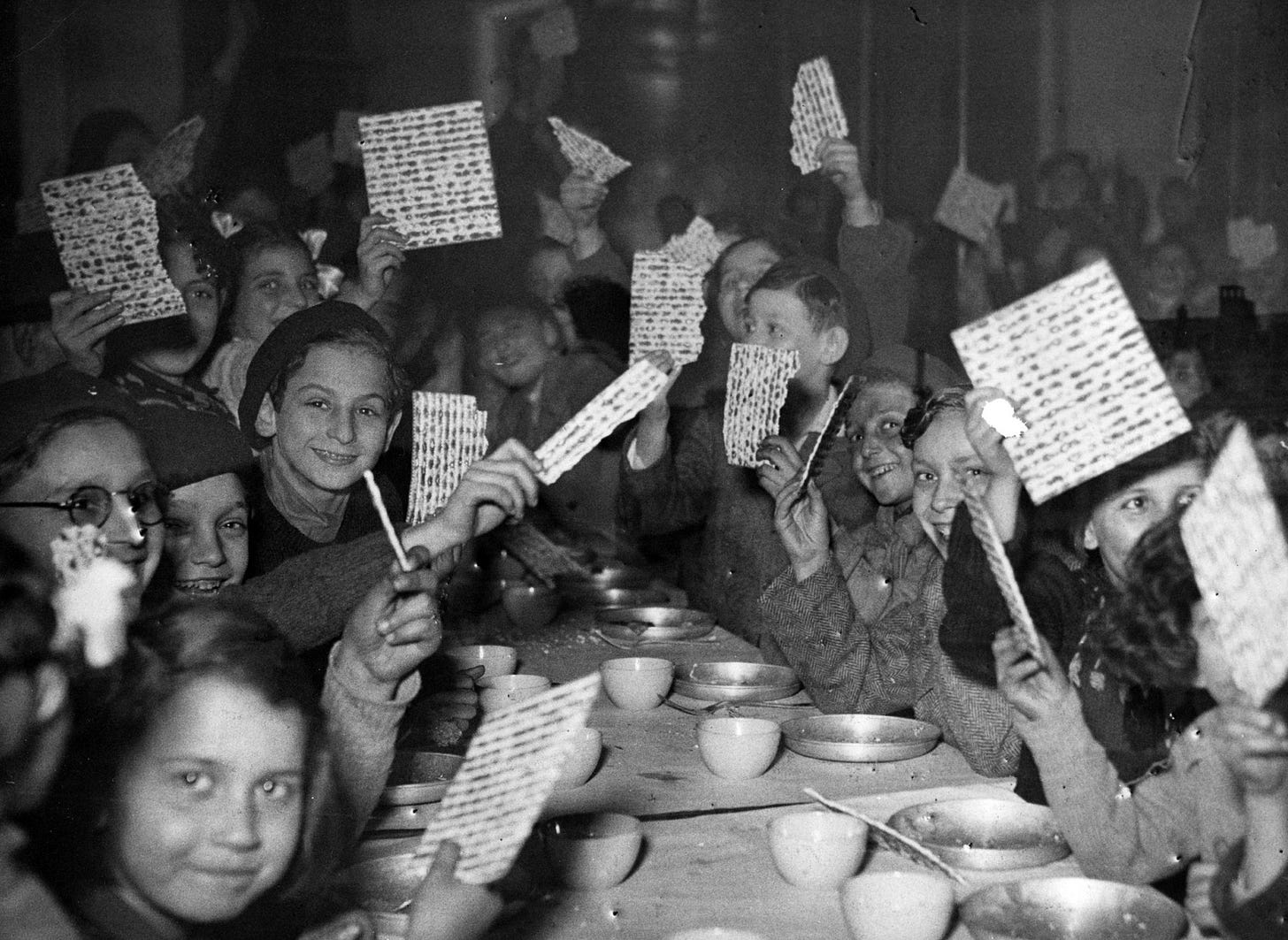 Young refugees at a Passover Seder holding up their matzot with pride at a children's canteen run by the JDC partner Federation des Societes Juives en France. France, c. 1947. Photographer unknown. Young refugees at a Passover Seder holding up their matzot with pride at a children's canteen run by the JDC partner Federation des Societes Juives en France. France, c. 1947. Photographer unknown.