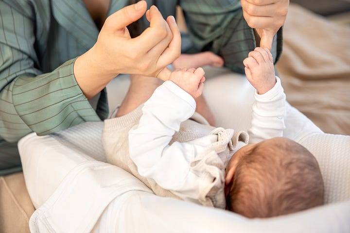 Hände halten Babyfüße und Baby hält sich an Fingern fest.